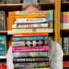 A portrait of Gavin Williams holding a pile of books in front of his face