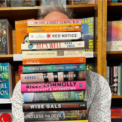 A portrait of Gavin Williams holding a pile of books in front of his face