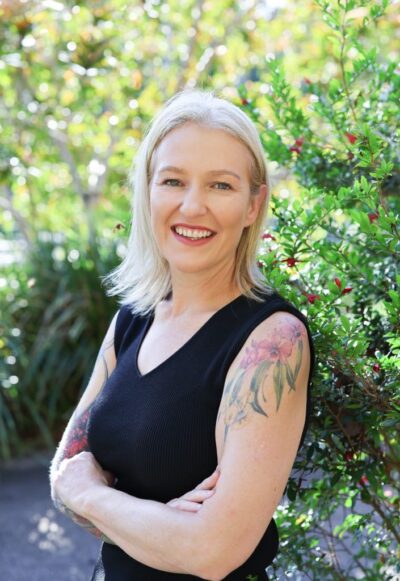 An image of Rebecca Ahola. She stands in front of greenery.