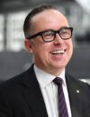 A photo of Alan Joyce smiling. He is wearing a suit and glasses.