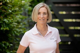 An image of Sarah Hawthorn. Sarah stands in front of a fence and greenery.