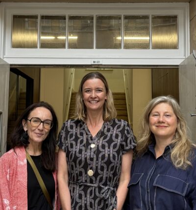 A photo of Courtney Collins, Jessie Ansons, and Rosemarie Milsom standing side-by-side before an open doorway.