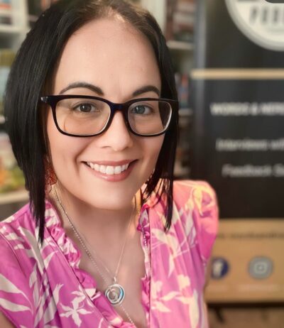 A photo of Dani Vee. Dani is wearing glasses and is smiling at the camera.